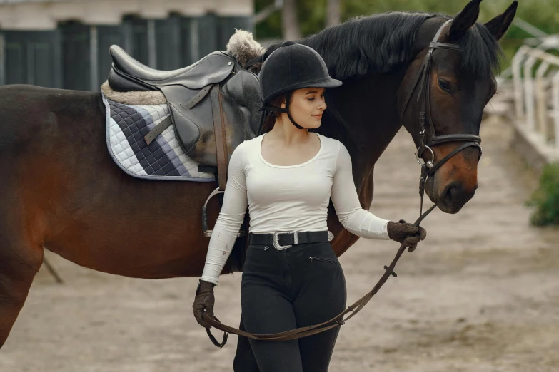 a young woman in riding gear is walking with her horse