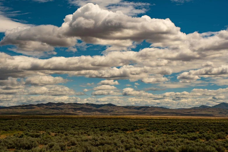 a few clouds flying over some hills and bushes