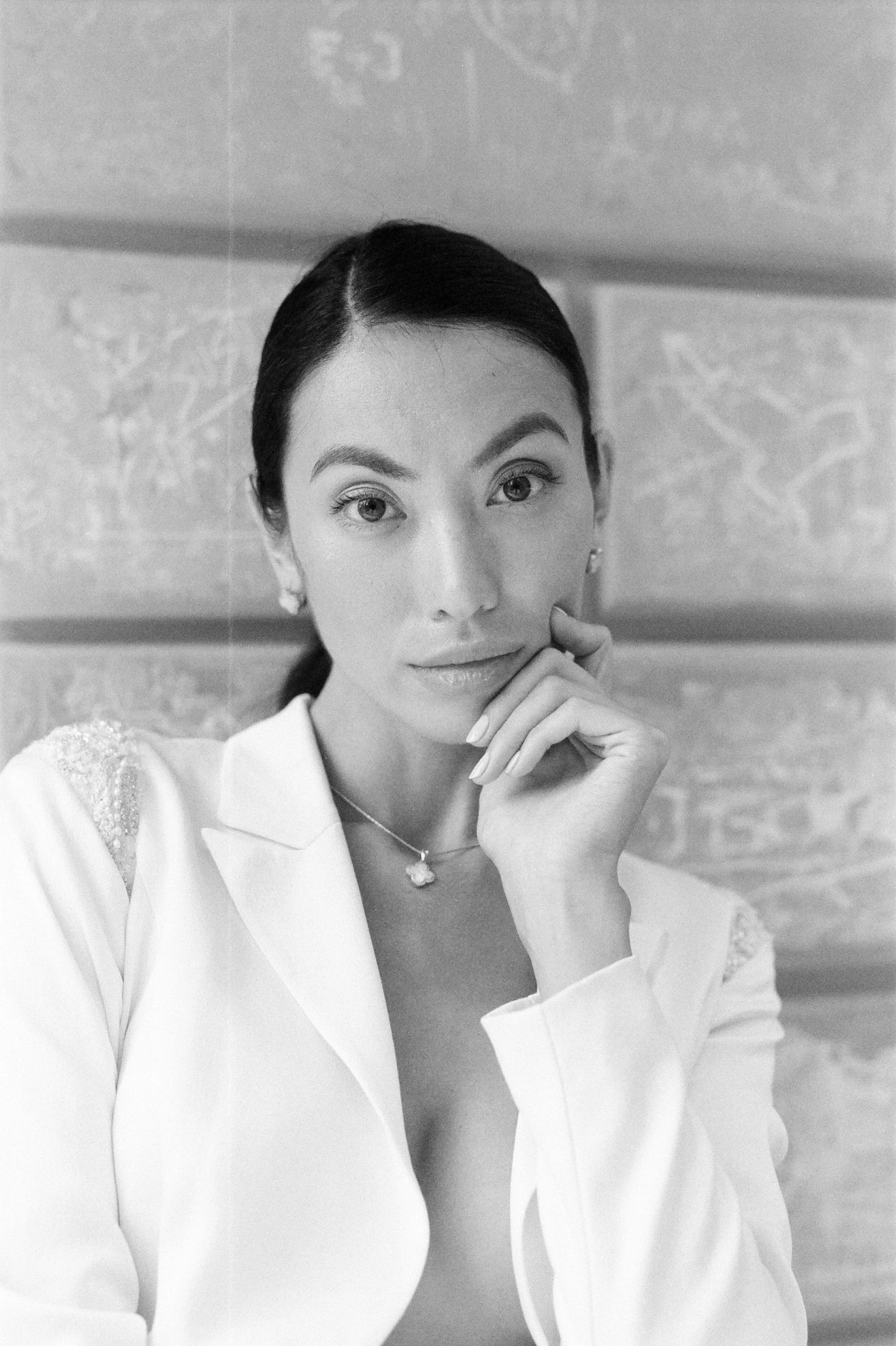 a woman posing for a po, wearing a white coat and sitting down