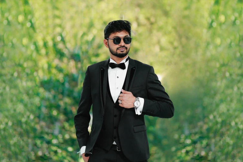 the man is posing in a tuxedo with sunglasses on