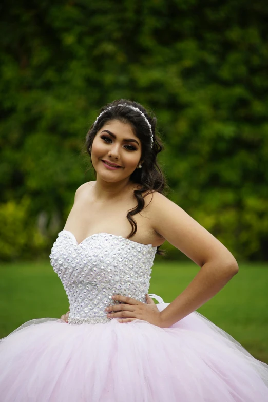 a beautiful young woman in pink ball gown standing next to trees