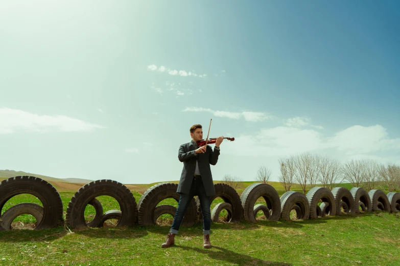a violin player leaning against a wall made out of tires