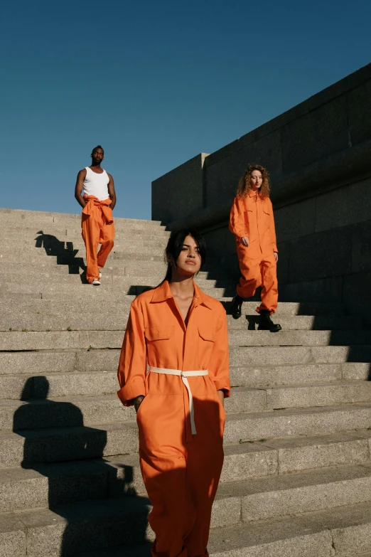 several people in orange prison jumpsuits walk up stairs