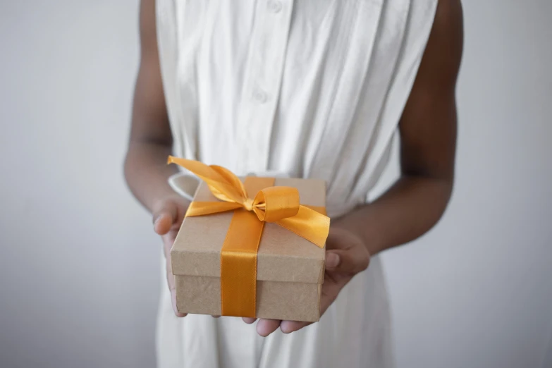 a woman wearing a dress holding up a present wrapped in brown paper