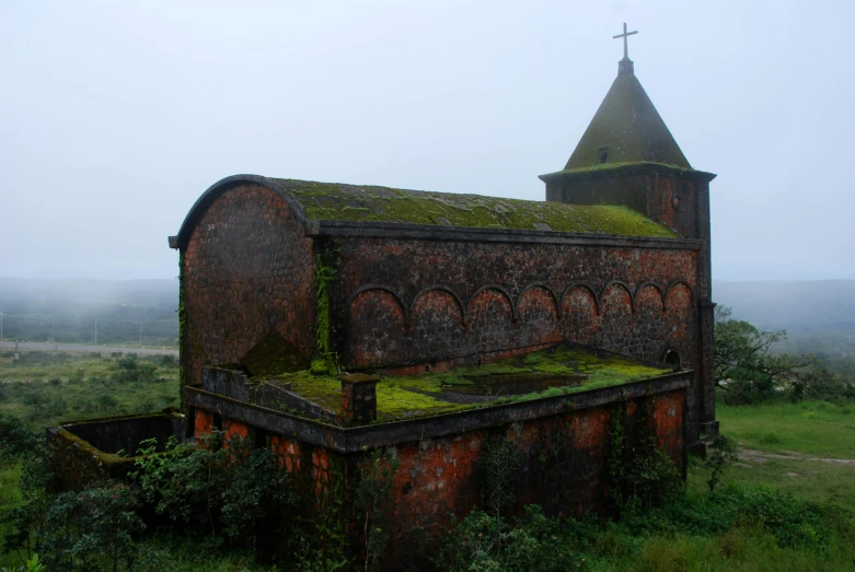 an old building sitting in a field near a cross