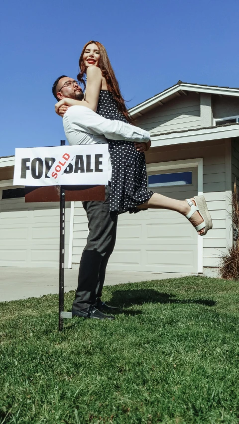 a couple are emcing next to a for sale sign