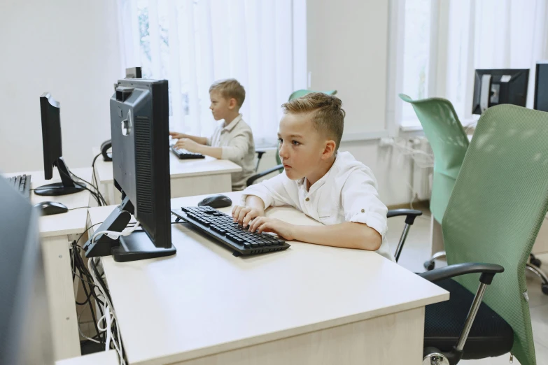 a boy sits at a computer while another works on the computer