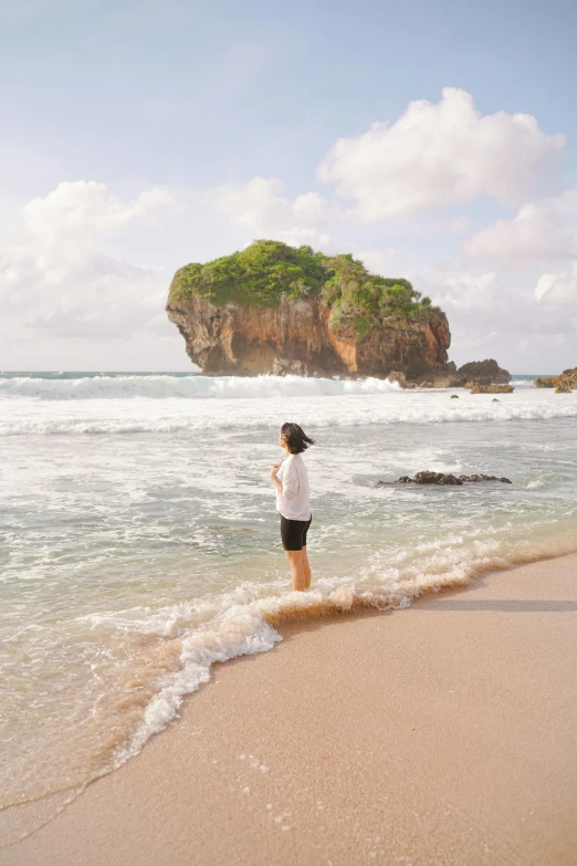 the person is standing in the ocean near the small island