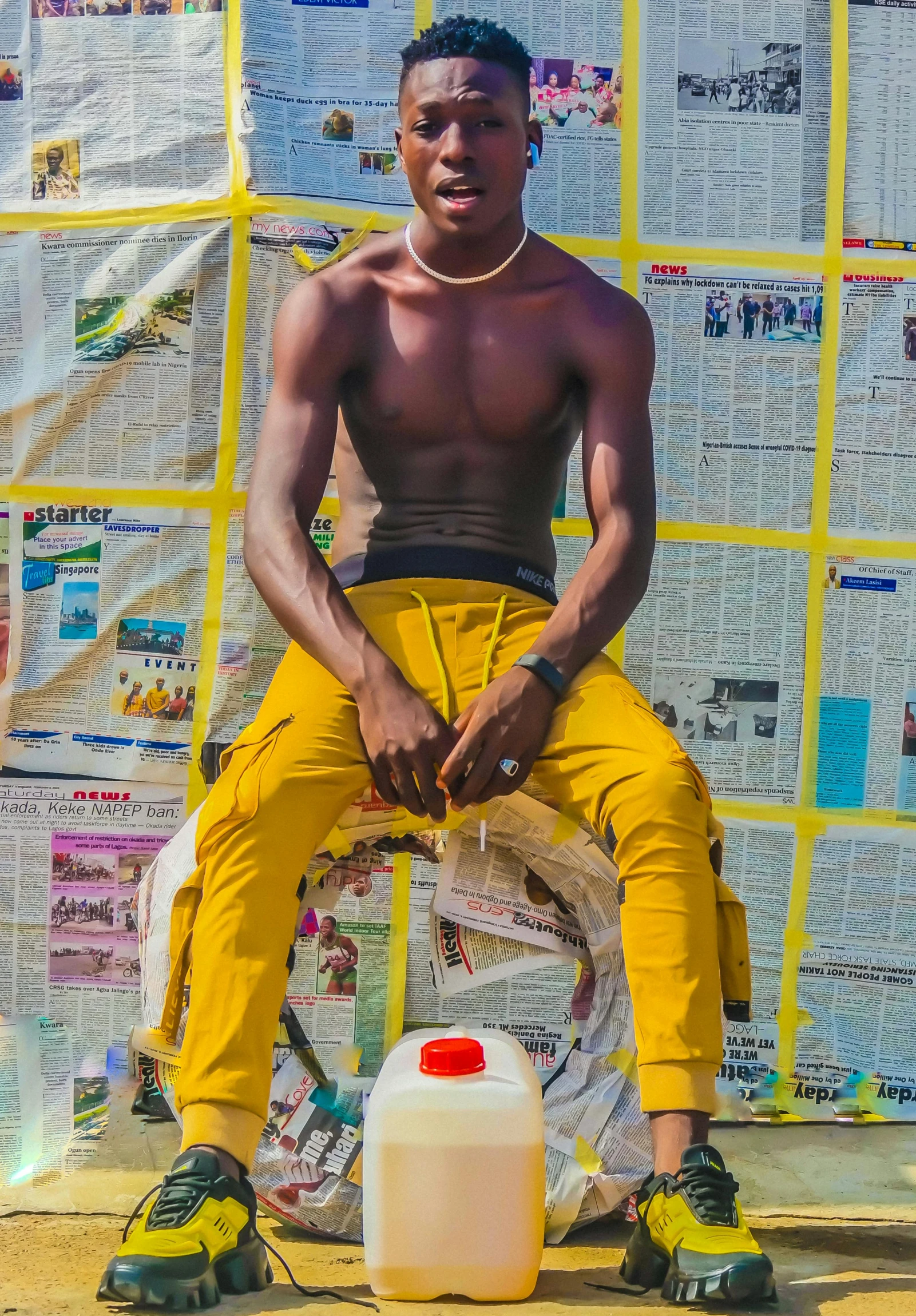 a man sits against a fence next to a wall with newspaper