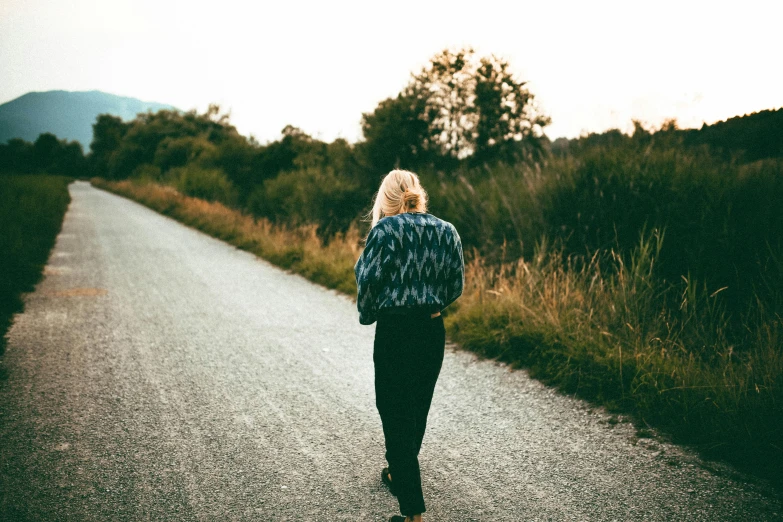 a person walking down a road in front of a green field