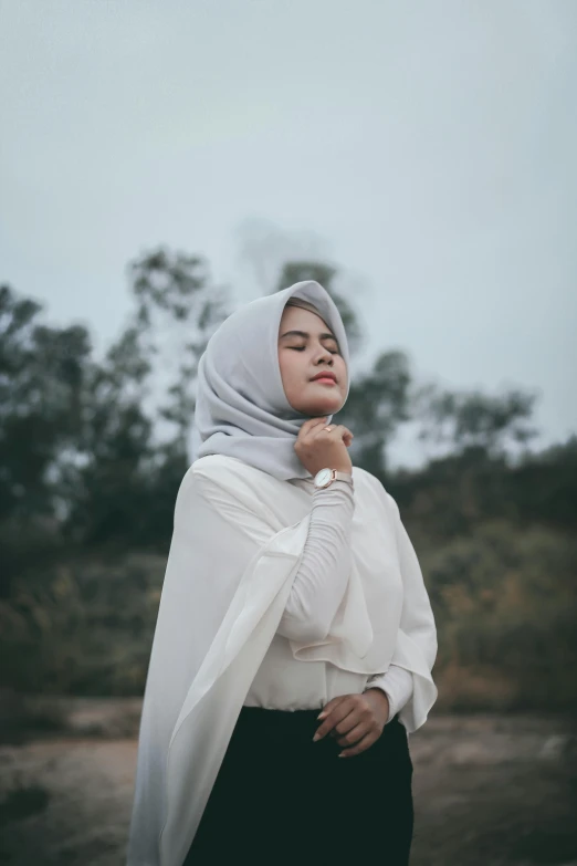 a woman wearing a white headdress standing near trees