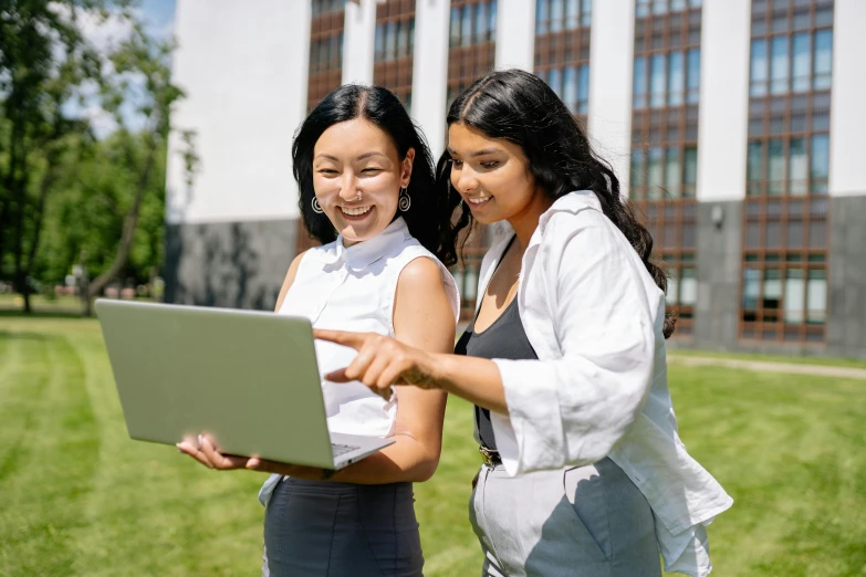 two girls looking at a laptop on the grass