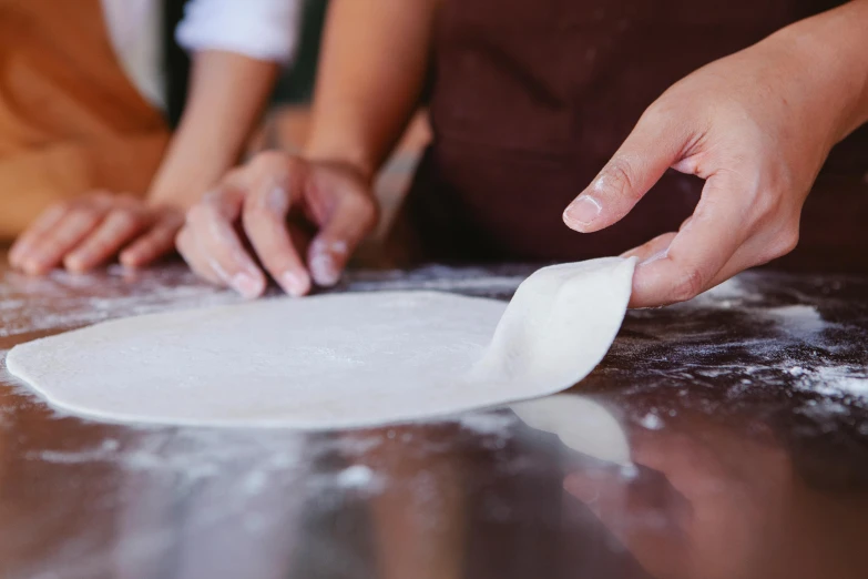 two people roll out dough from a pizza shell on a table