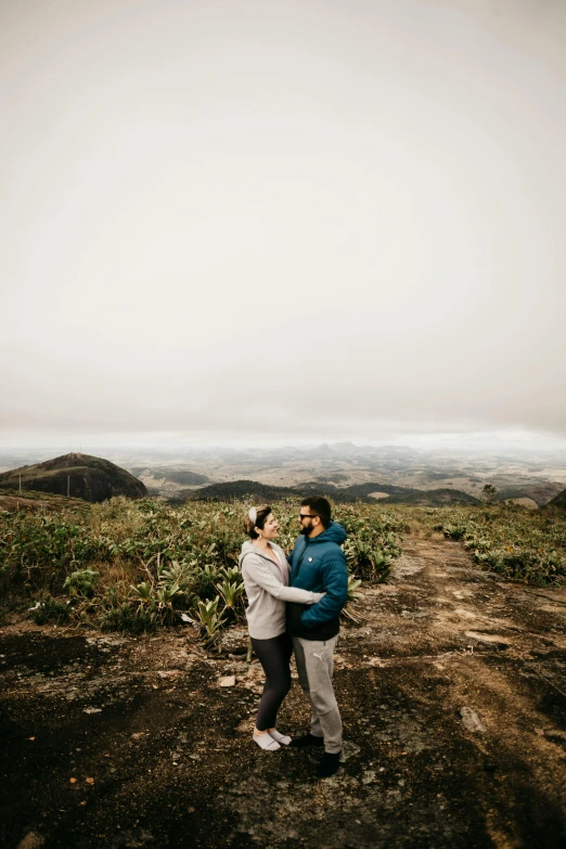 two people standing on a mountain top near a field