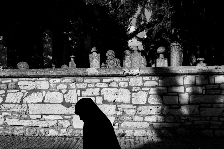 a person in silhouette walks down a sidewalk past a stone wall