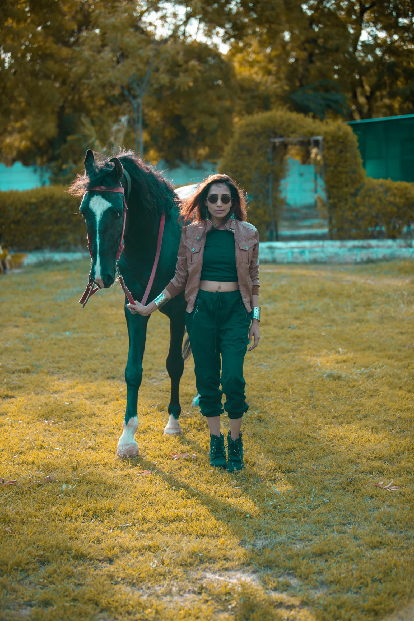 a girl with sunglasses walks a black horse in a field