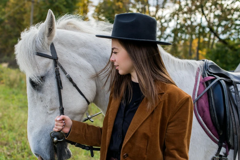 a woman in a black hat is petting a horse