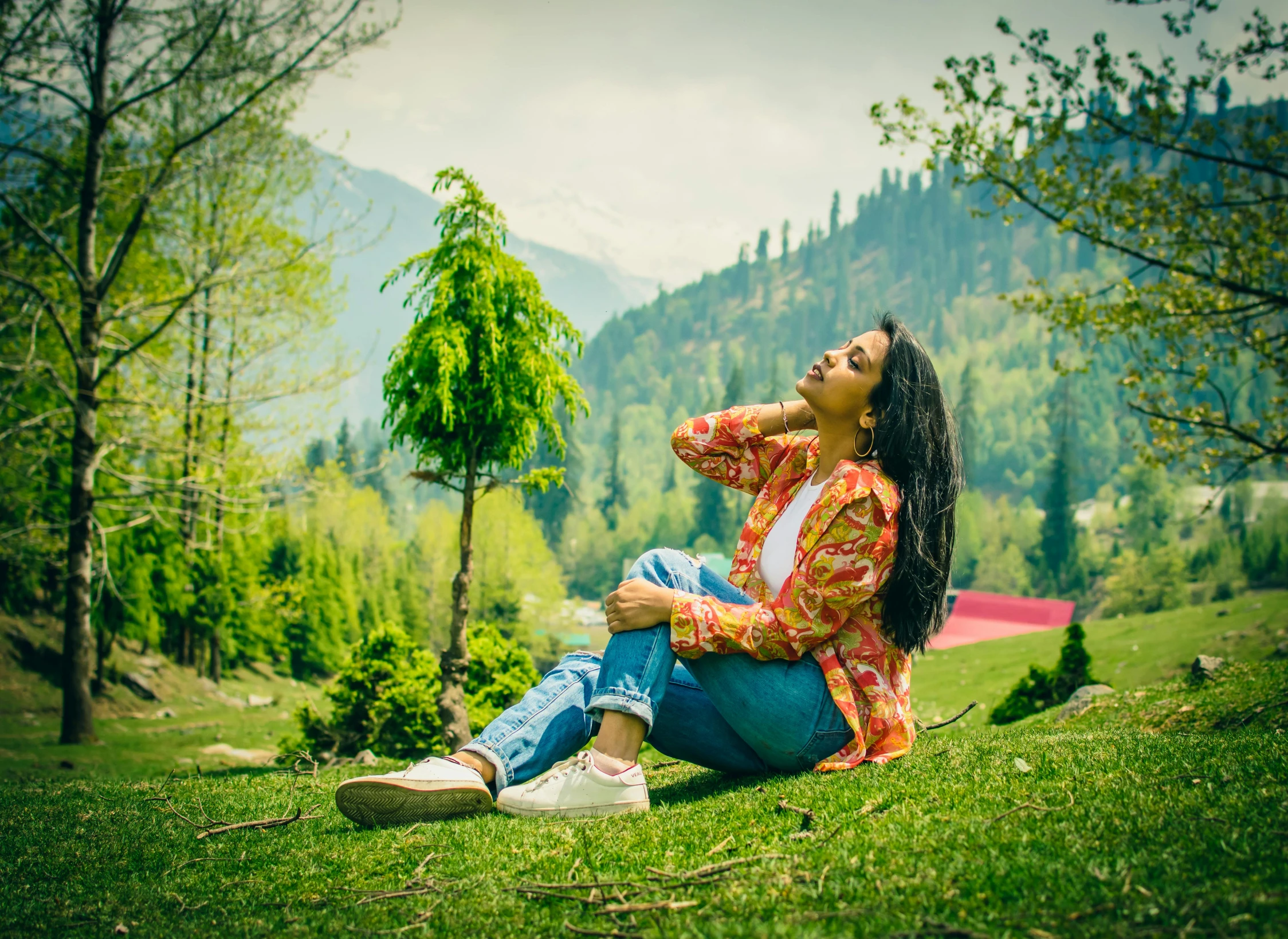 a young woman sitting on top of a green grass covered hillside