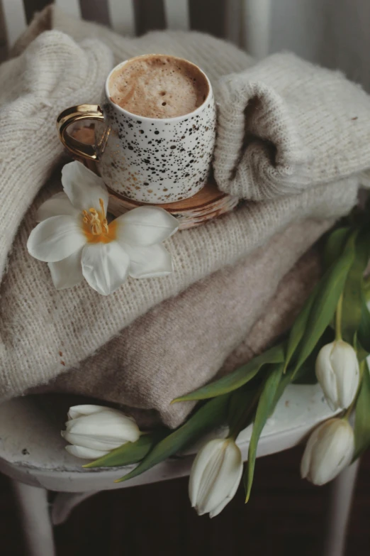 a cup of coffee sitting on top of a table next to white tulips