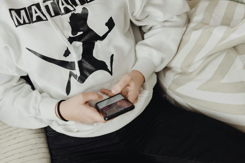 the person is wearing a white shirt with black graphic on it and holding a cell phone