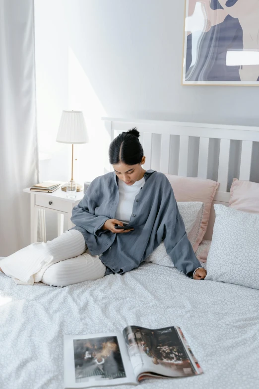 a woman sitting on her bed and texting on her phone