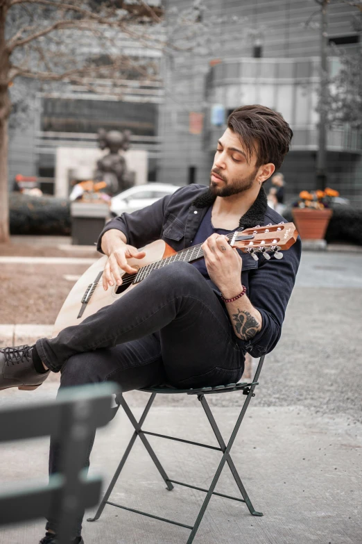 a man that is sitting on a folding chair playing the guitar