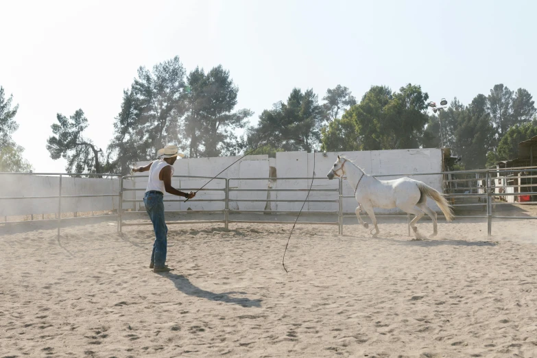 man in cowboy hat leading a white horse in a corral