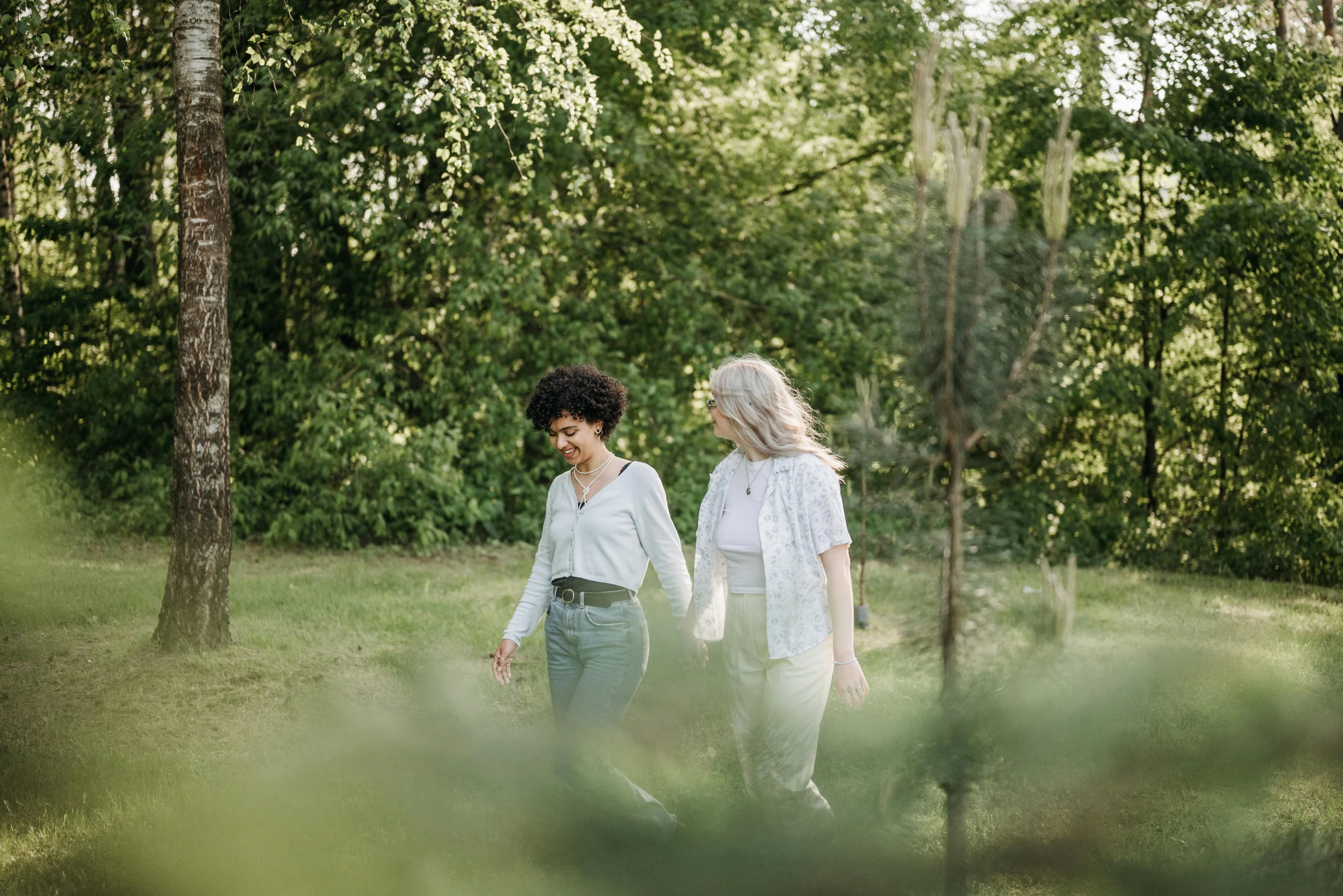 two women holding hands walking in a wooded area