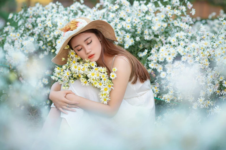 a woman sitting in front of white flowers wearing a hat