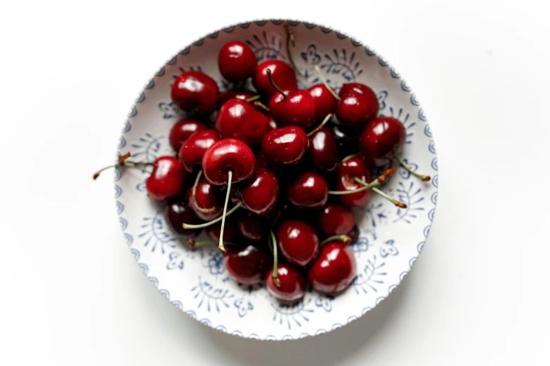 a white bowl full of cherries on a white surface