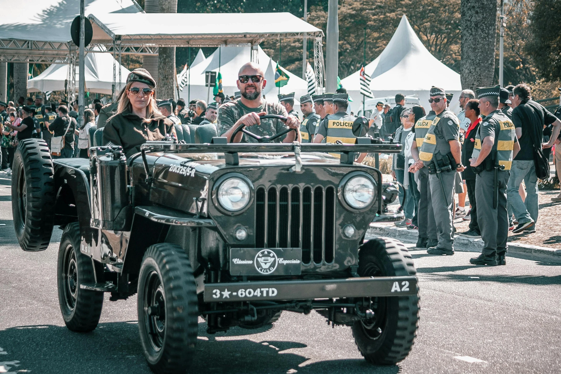 people are watching a jeep drive down a street with two men riding on it