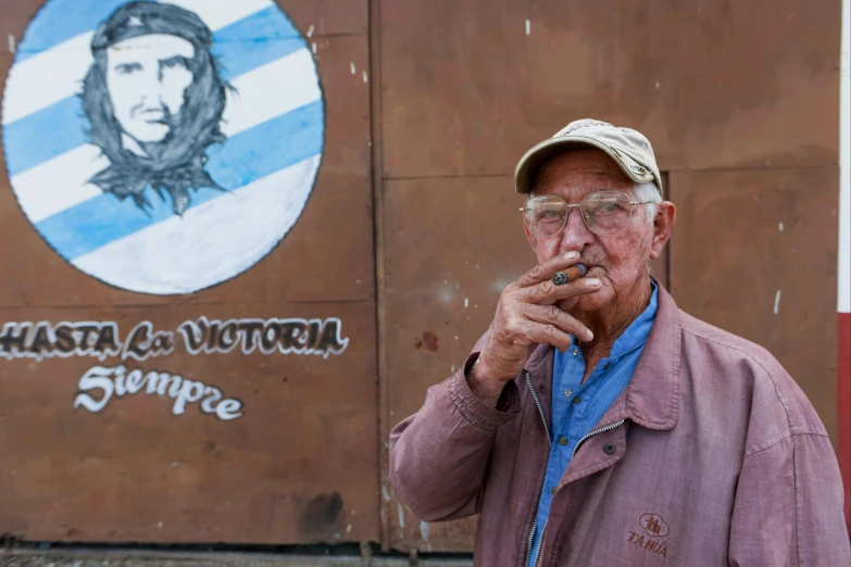 an elderly man smoking a cigar while wearing a hat