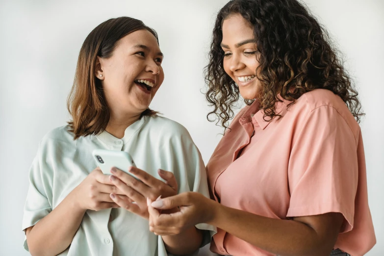 two women laugh while holding up a tablet computer