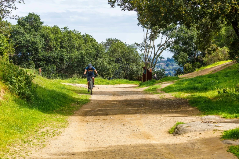 there is a man on a bicycle coming up a dirt trail