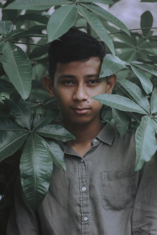 a boy is looking through leaves with a serious look on his face