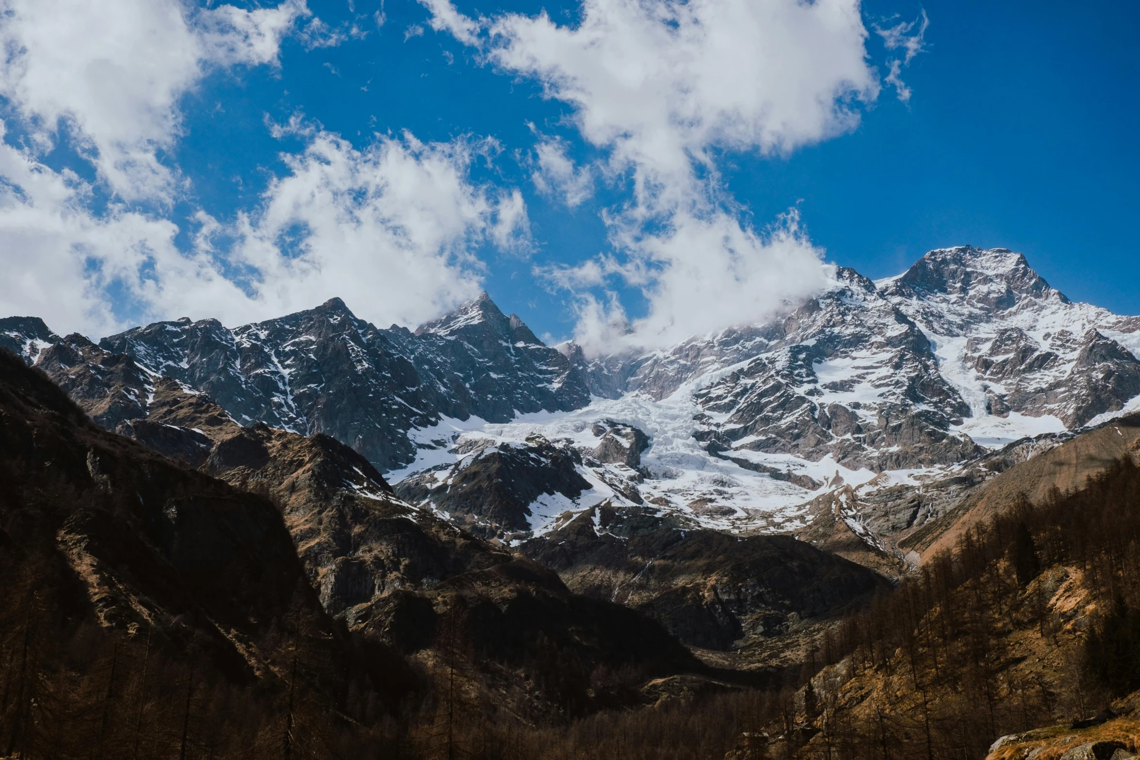 the mountainside is covered in snow as clouds hang over