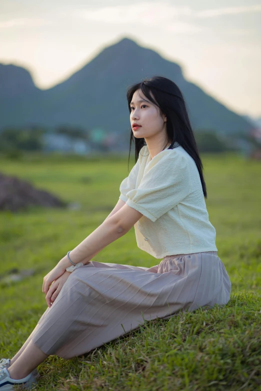 an asian woman sits on the grass in front of a mountain