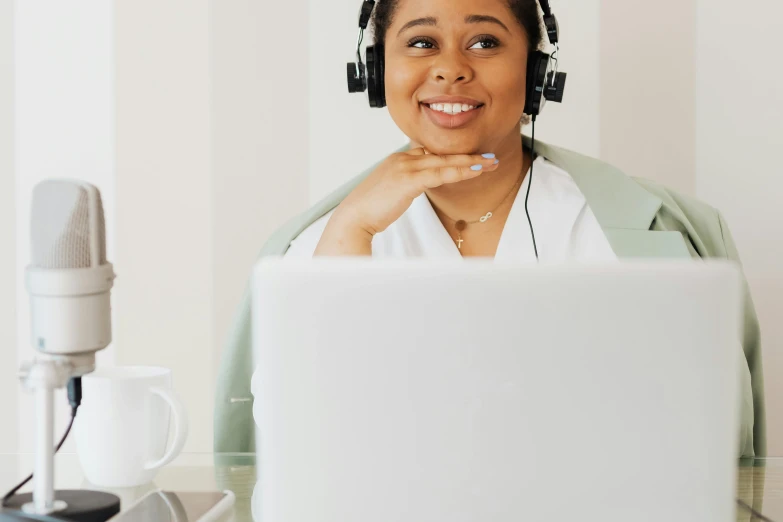 a smiling black woman wearing headphones is in front of a laptop