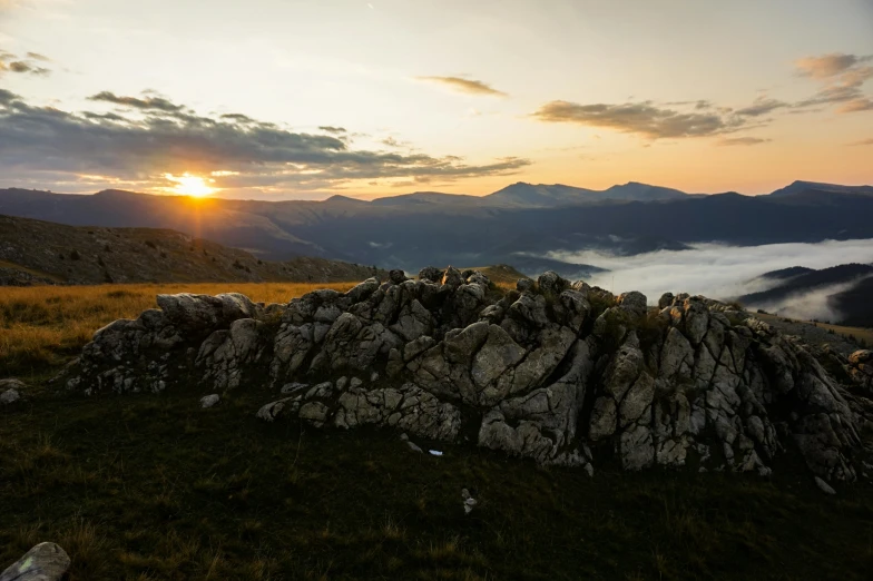 the sun setting on the mountain, with rocks piled together