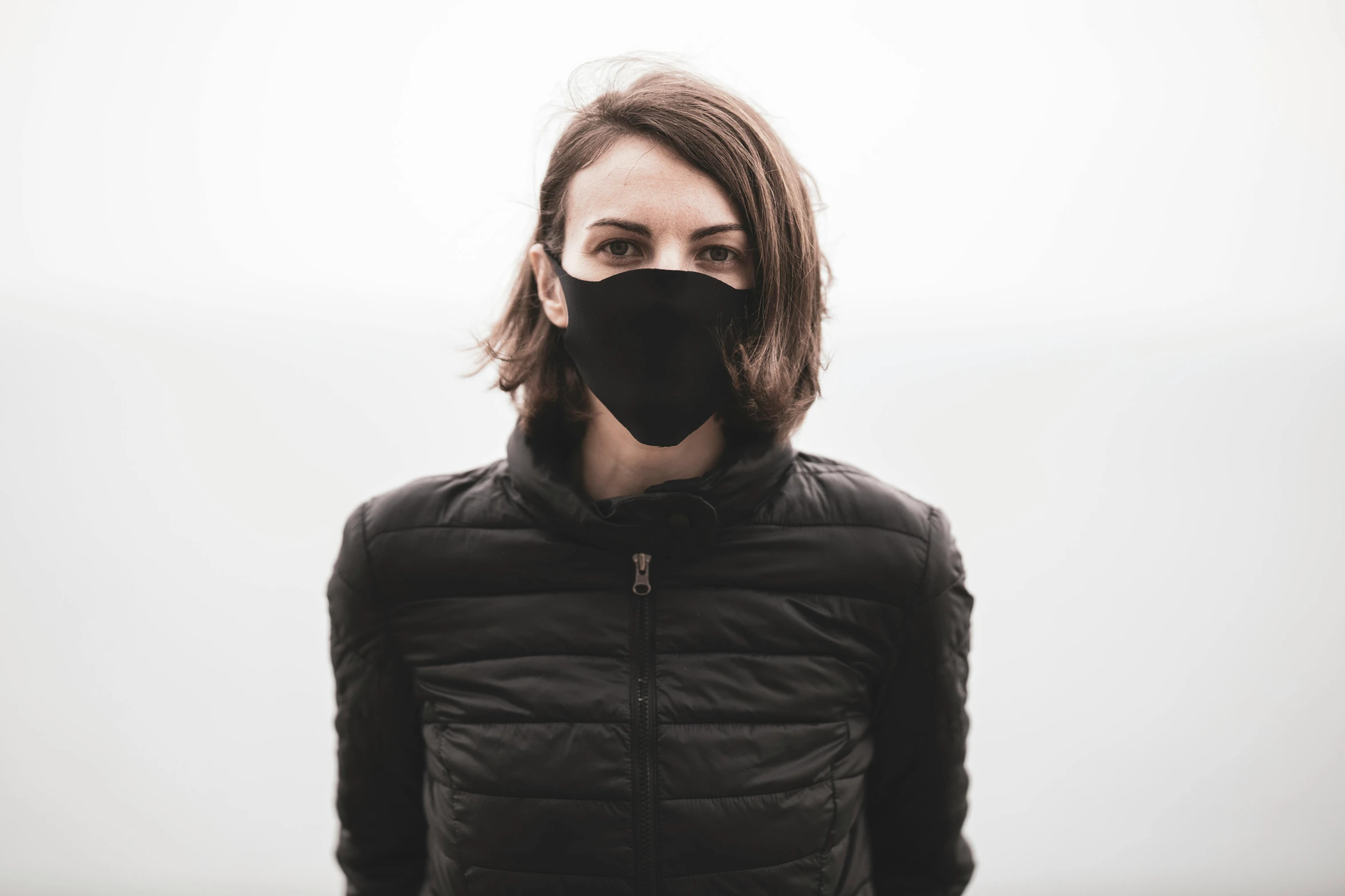 woman wearing black mask and jacket standing in front of white background