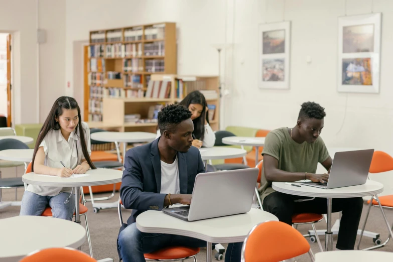 four students sit at tables on their laptops