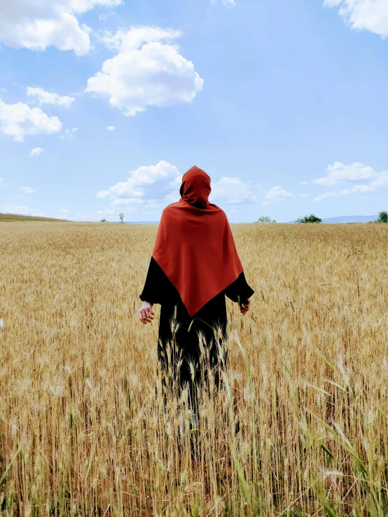 woman in red cape walking through a field of tall grass