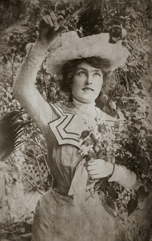 a woman standing in front of bushes with a hat