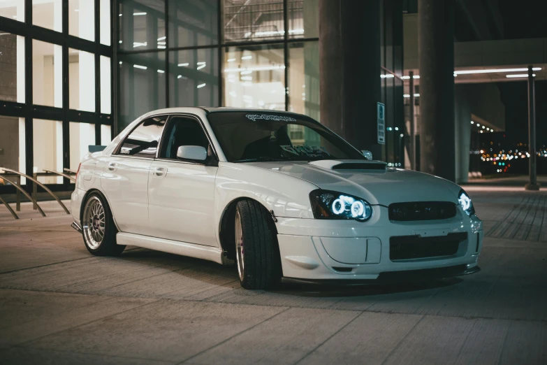 a white car parked next to a tall building at night