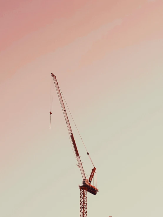 two cranes on top of a large building against a pale blue sky