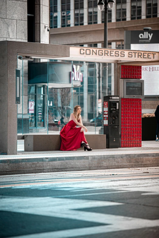 a woman in a red dress sitting on the sidewalk in front of a building