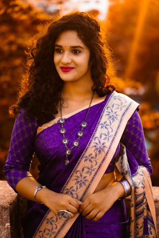 a woman in a purple saree smiling and holding her hands folded