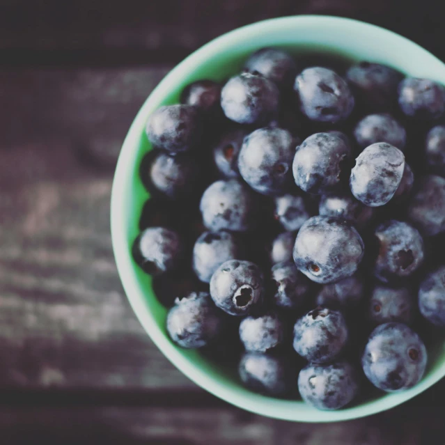 a green bowl full of blueberries sits on a wood table