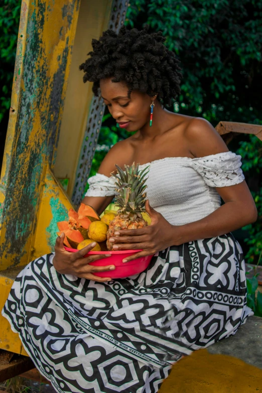 a woman is sitting down holding a bowl of fruits