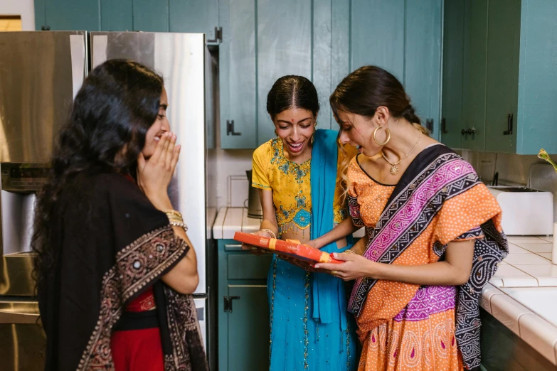 three woman in colorful saris are holding a package